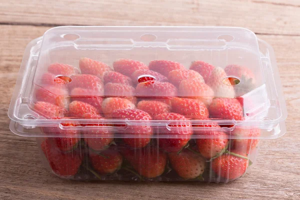plastik kutu ambalaj ahşap masa üzerinde kırmızı olgun çilek