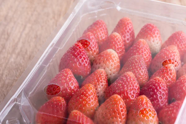 Red ripe strawberry in plastic box of packaging on wood table — Stock Photo, Image