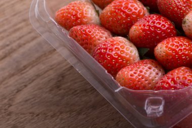 plastik kutu ambalaj ahşap masa üzerinde kırmızı olgun çilek