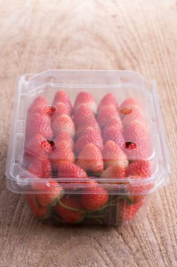 plastik kutu ambalaj ahşap masa üzerinde kırmızı olgun çilek