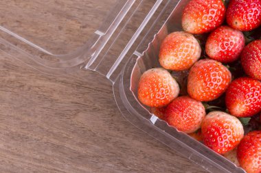 plastik kutu ambalaj ahşap masa üzerinde kırmızı olgun çilek