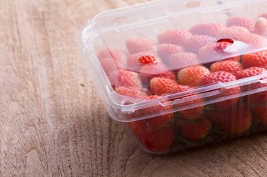 plastik kutu ambalaj ahşap masa üzerinde kırmızı olgun çilek