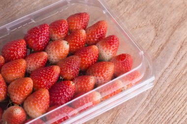 plastik kutu ambalaj ahşap masa üzerinde kırmızı olgun çilek