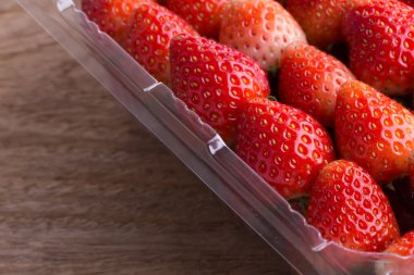 plastik kutu ambalaj ahşap masa üzerinde kırmızı olgun çilek