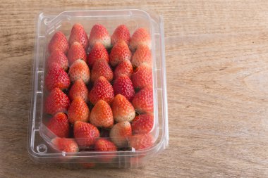 plastik kutu ambalaj ahşap masa üzerinde kırmızı olgun çilek