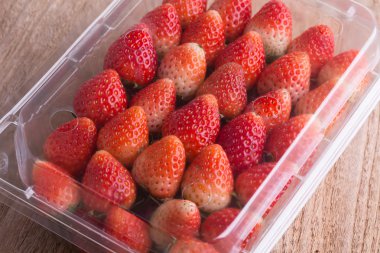 plastik kutu ambalaj ahşap masa üzerinde kırmızı olgun çilek