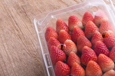 plastik kutu ambalaj ahşap masa üzerinde kırmızı olgun çilek