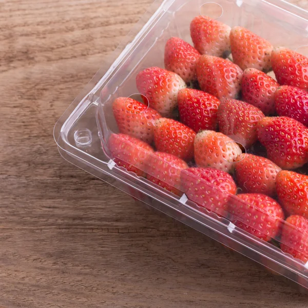 Rote reife Erdbeere in Plastikverpackung auf Holztisch — Stockfoto