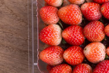 plastik kutu ambalaj ahşap masa üzerinde kırmızı olgun çilek