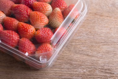 plastik kutu ambalaj ahşap masa üzerinde kırmızı olgun çilek