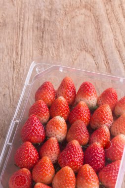 plastik kutu ambalaj ahşap masa üzerinde kırmızı olgun çilek