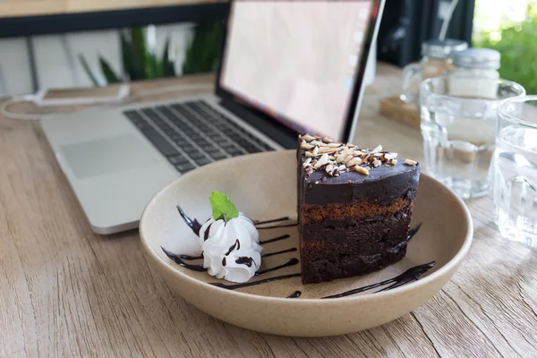 Cioccolato torta sul lavoro tavolo di legno con computer portatile notebook — Foto Stock