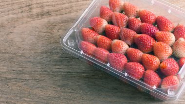 plastik kutu ambalaj ahşap masa üzerinde kırmızı olgun çilek