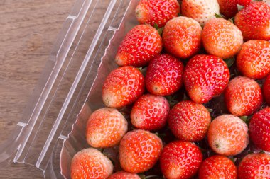 plastik kutu ambalaj ahşap masa üzerinde kırmızı olgun çilek