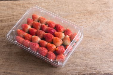 plastik kutu ambalaj ahşap masa üzerinde kırmızı olgun çilek