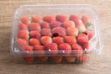 plastik kutu ambalaj ahşap masa üzerinde kırmızı olgun çilek