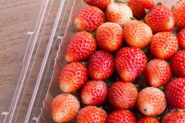 plastik kutu ambalaj ahşap masa üzerinde kırmızı olgun çilek