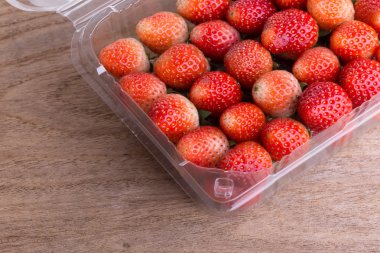 plastik kutu ambalaj ahşap masa üzerinde kırmızı olgun çilek