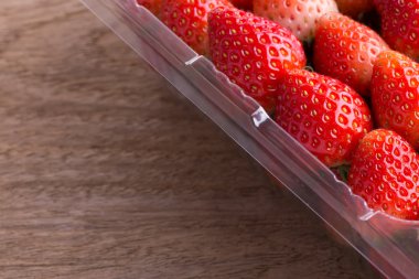 plastik kutu ambalaj ahşap masa üzerinde kırmızı olgun çilek