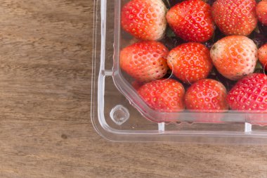 plastik kutu ambalaj ahşap masa üzerinde kırmızı olgun çilek