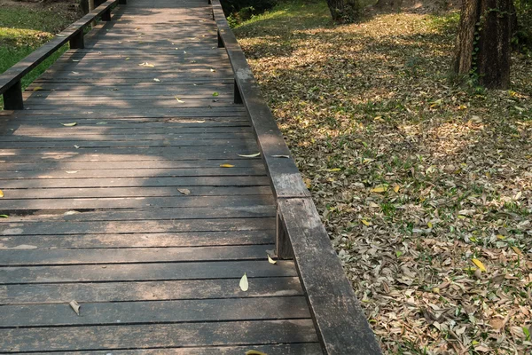 Старая деревянная дорожка с опадающими листьями утром осени — стоковое фото