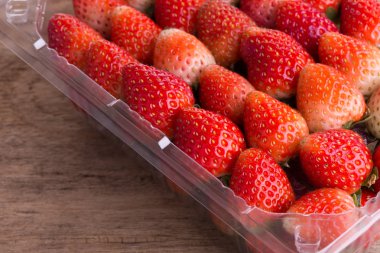 plastik kutu ambalaj ahşap masa üzerinde kırmızı olgun çilek