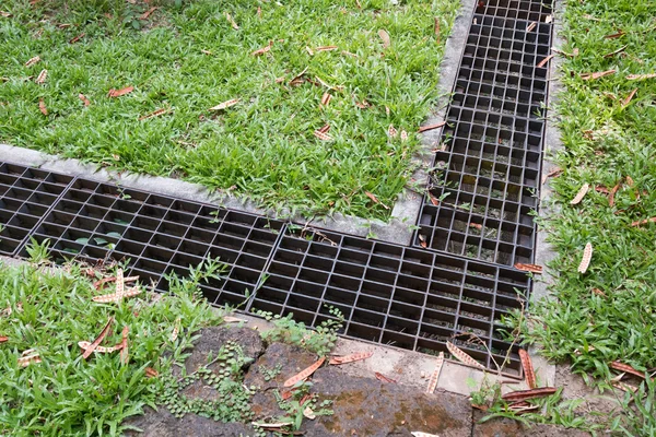 Iron grate of water drain in grass garden field — Stock Photo, Image