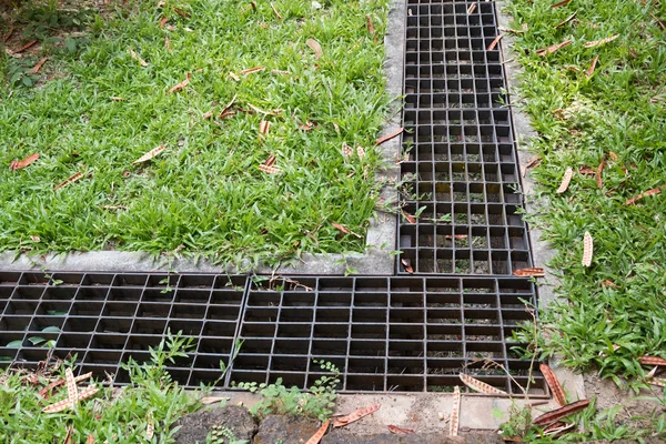 Iron grate of water drain in grass garden field — Stock Photo, Image