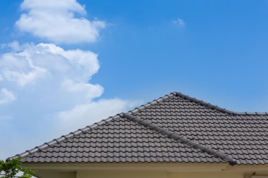 black tile roof of house with blue sky and cloud background clipart