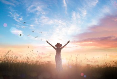 Praise and worship God concept: Silhouette of healthy woman raised hands at meadow sunset background clipart