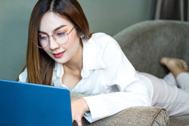 Ev konsepti: Güzel Asyalı kadın oturma odasında çalışırken dizüstü bilgisayar kullanıyor