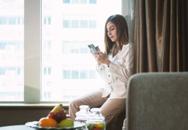 Ev konsepti: Güzel Asyalı kadın oturma odasında çalışırken akıllı telefon kullanıyor.