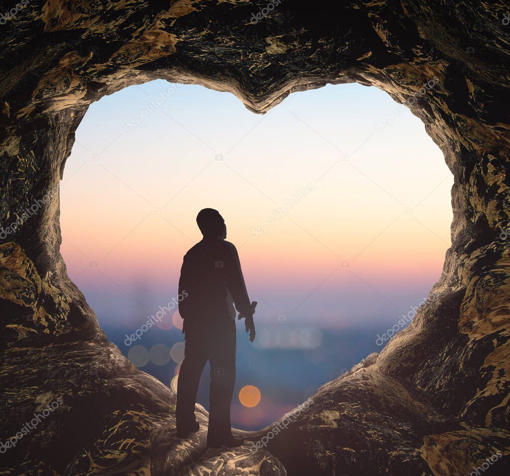 Worship God concept: Silhouette human standing on cave of heart against blurred city sunrise background