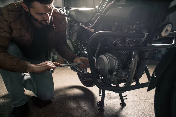 Young man wearing leather jacket fixing the motorcycle in garage. Man's hobby concept