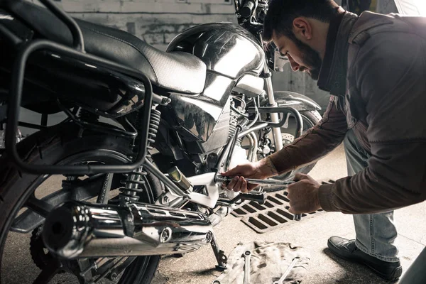 ガレージでバイクを修理する革のジャケットを着た若い男 男の趣味の概念 ストック写真