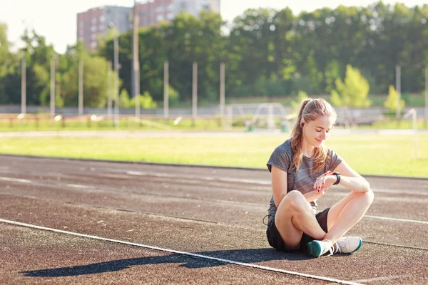 スポーティ女の子チェック彼女のパルスながら座っている間に実行中のトラック ロイヤリティフリーのストック写真