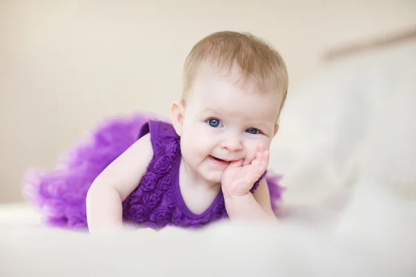 Baby girl in a purple dress lying on the bed — Stock Photo, Image