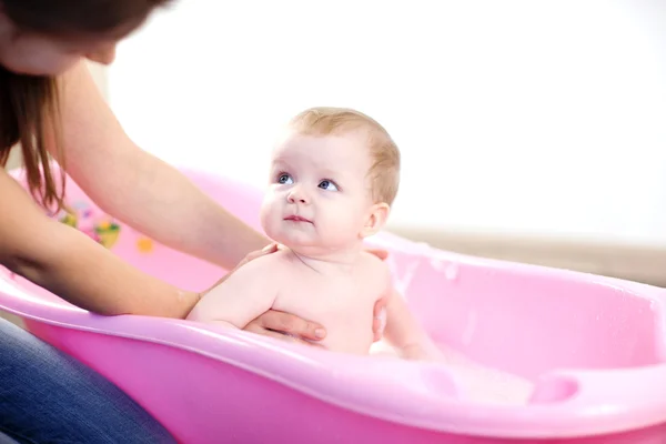 Мама стирает ребенка в розовой ванне — стоковое фото
