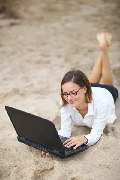 Woman working while lying on a sand — Stock Photo, Image