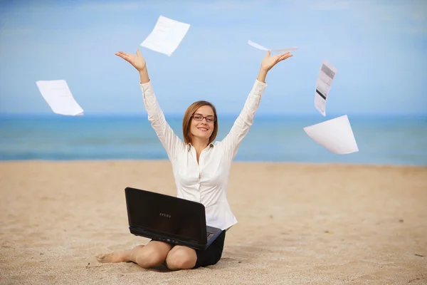 Bir dizüstü bilgisayar ile bir plajda çalışan genç iş kadını gülümseyen