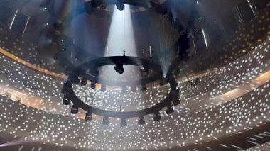 Sahne ışıkları dairesel sahnenin üstündeki metal yapılar üzerinde yer alıyor ve ışık huzmeleri yayıyor..