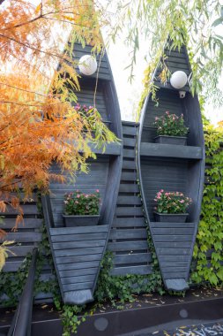 Ivy, küçük dekoratif teknelerin ahşap raflarda durduğu bir iç mekanı çerçeveleyerek güneşli bir duvar boyunca yavaşça taşar. Yumuşak ışık, doğal dokular ve yumuşak yeşillik barışçıl ve nostaljik bir deniz atmosferi yaratır.