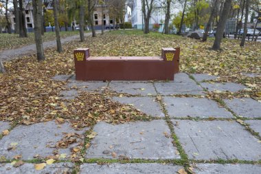 Altın yapraklar ve yumuşak güneş ışığıyla çevrili bir sonbahar parkında, açık bir kapının yanında duran yalnız bir bank. Sahne gizemli ama huzurlu, sıcaklıkla, sessizlikle ve değişimin güzelliğiyle dolu.