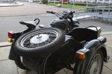 Eski model siyah motosikletli bir motosiklet açık bir sergide gururla duruyor, klasik tasarım, zamansız stil ve mekanik işçilik sergileniyor..