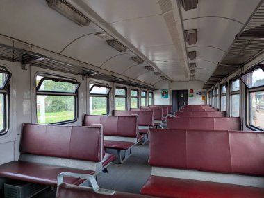 Boş bir banliyö vagonunun içi, temiz koltuklar ve tırabzanlar, pencerelerden geçen doğal ışık, modern ulaşım ortamı, sakin kentsel seyahat sahnesi..