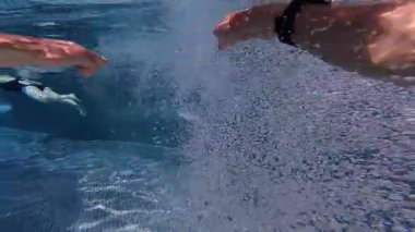 Bir adam berrak bir havuzda zarif bir şekilde yüzer. Suyun içinden süzülen ışıkla birlikte sakin ve akışkan bir sahne yaratır..