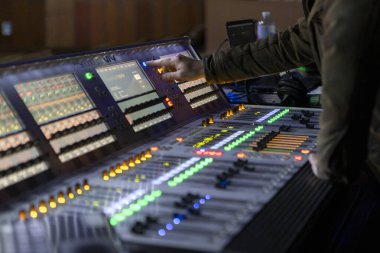 Bir ses mühendisi konser sırasında dijital karıştırma konsolunda çalışır, canlı sahne ışıkları kontrol yüzeyini aydınlatırken seviyeleri ve efektleri ayarlar ve canlı ses üretiminin dinamik bir sahnesini yaratır..