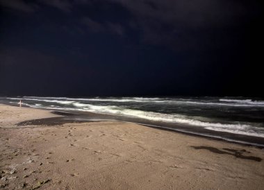 Deniz yumuşak, ritmik dalgalar oluşturur pürüzsüz kumu, gece görüşünü yıkar.