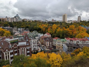 Zamkova Hora 'dan Kyiv' in merkez kısmının sonbahar manzarası, altın ağaçlar, tarihi çatılar ve yumuşak mevsimlik ışıklarla çerçevelenmiş şehrin ufuk çizgisini gösteriyor ve şehir manzarasının üzerinde sakin bir panoramik manzara yaratıyor..