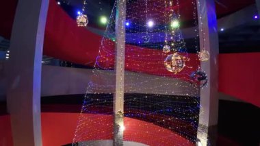 Bir binanın içinde, parlayan çelenklerden şekillendirilmiş bir Noel ağacı dinamik ışıklandırma efektleri ve görsel simetrisi olan modern bir tasarım nesnesi olarak görünür..